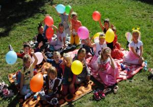 dzieci z gr. VI z żółtymi balonami siedzą na kocu w ogrodzie